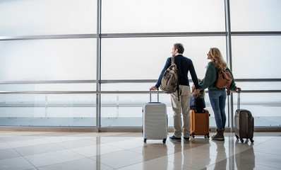 Satisfied man, woman and girl looking out from big window at the airport. They are taking pleasure in airplanes moving along the runway. Copy space in left side