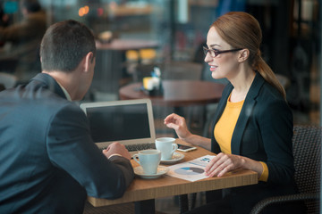 Poster - Outgoing female telling with colleague while sitting at table in cafe. They working with notebook computer. Labor and technology concept