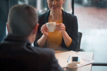 Aufkleber - Outgoing woman drinking mug of appetizing beverage while telling with comrade in cafe. Affiliate turning back to camera. Lunch concept