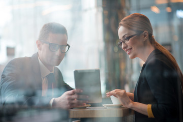 Poster - Portrait of outgoing male and happy businesswoman looking at electronic tablet. Cheerful colleagues sitting at desk. Comrades indoor. Job concept