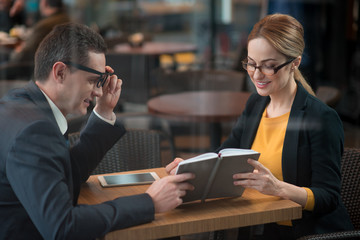 Poster - Glad businessman and outgoing female looking through day planner while situating at desk indoor. Job and rest concept