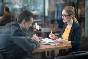 Poster - Side view friendly female telling with happy businessman while locating at table in cafe. She making notes. Conversation and work concept