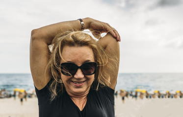 Close up of smiling older woman (70-79)  stretching triceps at beachside in Rio de Janeiro, Brazil