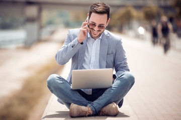 Wall Mural - Young attractive man sitting on concrete while using cell phone.