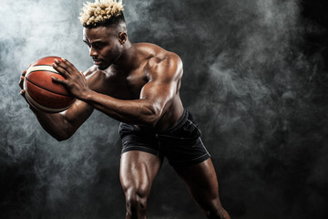 Portrait of afro-american sportsman, basketball player with a ball over black background. Fit young man in sportswear holding ball.