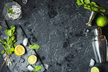 Wall Mural - Mojito cocktail making. Mint, lime, glass, ice, ingredients and shaker on black stone background