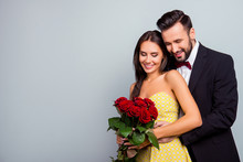 Portrait Photo With Copy Space Of Charming, Lovely, Cute Couple In Formal Wear, Dress Hugging And Looking At  Bouquet Of Red Roses, Wife And Husband Celebrating  14 February On Grey Background