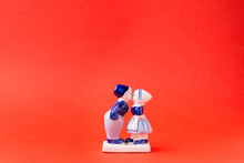 Porcelain Figurines Of Kissing Boy And Girl In National Dutch Costumes On Red Background. Saint Valentine's Day Concept.