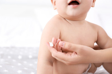 Woman applying body cream on her baby against light background