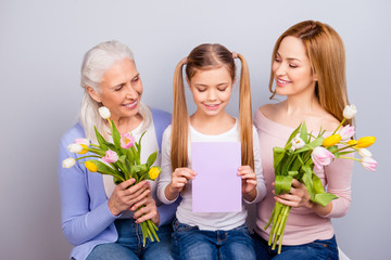 Sticker - Parenthood childhood motherhood maternity tenderness warmth international beauty concept. Three lovely cute sweet beautiful gentle women holding flowers and card looking down isolated gray background