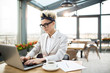 © pressmaster - Young elegant businesswoman working in the net while sitting in cafe