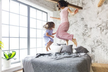Family Fun. Mother And Daughter Jumping On The Bed