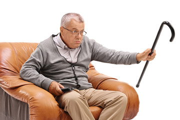 Sticker - Annoyed senior with a cane sitting in an armchair and watching television