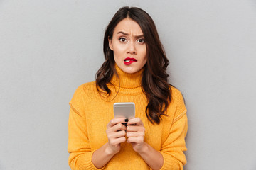 Sticker - Worried brunette woman in sweater with smartphone bites her lip