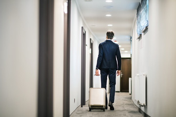 Wall Mural - Mature businessman walking with luggage in a hotel corridor.