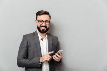Smiling man in white shirt typing text message or scrolling feed in social network using smartphone, over gray background