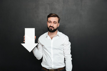 Canvas Print - Picture of pessimistic upset man 30s holding blank speech arrow pointer directing downward, over dark gray wall copy space