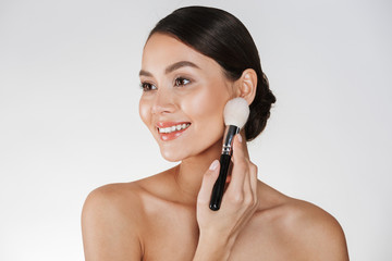 Canvas Print - Beauty picture of attractive woman with perfect smile looking aside and applying makeup using brush, isolated over white background