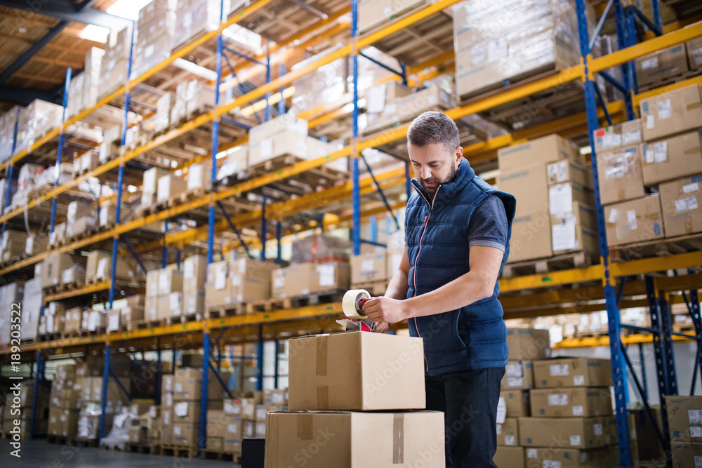 Male warehouse worker sealing cardboard boxes. Stock Photo | Adobe Stock