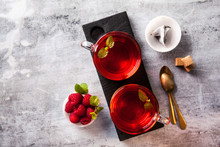 Hot Raspberry Tea In Two Transparent Cups On A Stone Table. Fresh Berries, Cubes Of Cane Sugar And A Bag Of Tea. Copy Space