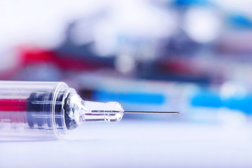 Macro of syringe injection with pile of syringes in the background, pharmaceutical concept