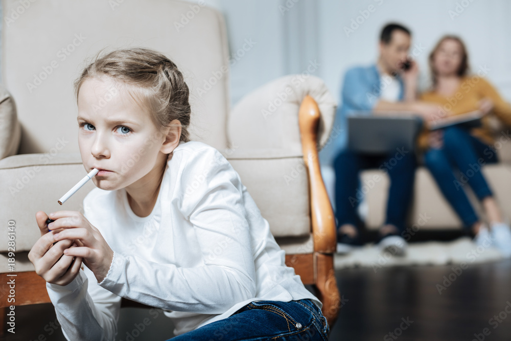 daughter smoking cigarettes Cigarette. Poor blue-eyed little girl holding a cigarette and smoking while  her parents working on their laptops Stock Photo