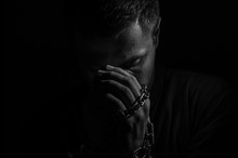 Repented Man Prisoner With His Hands Shackled In Chains On A Dark Background