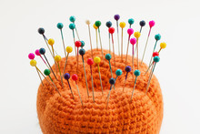 Multicolored Sewing Pins In The Orange Pin Cushion On Light Background. Closeup, Selective Focus
