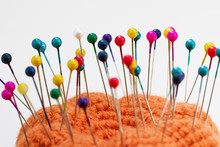 Multicolored Sewing Pins In The Orange Pin Cushion On Light Background. Closeup, Selective Focus