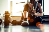 Fototapeta  - Sport woman sitting and resting after workout or exercise in fitness gym with protein shake or drinking water on floor. Relax concept. Strength training and Body build up theme. Warm and cool tone