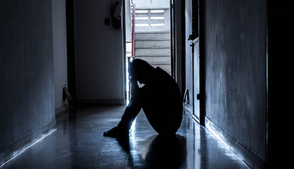 Silhouette of a sad young man sitting in the dark leaning against the wall with his back, The sun is in sorrow.