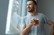 © Viktoriia - Bachelor man daily routine standing near the window single lifestyle concept drinking tea dreaming