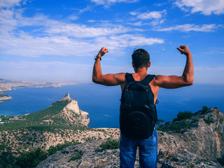 Wall Mural - man traveler with backpack standing with his back to the precipice of the mountain