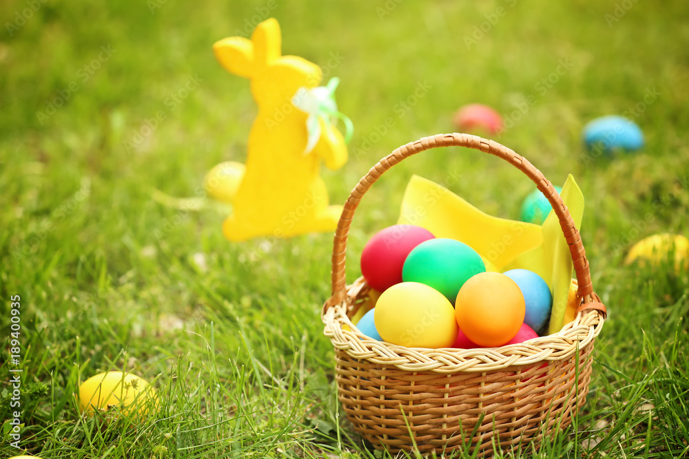Colorful eggs in wicker basket on green grass. Easter hunt concept