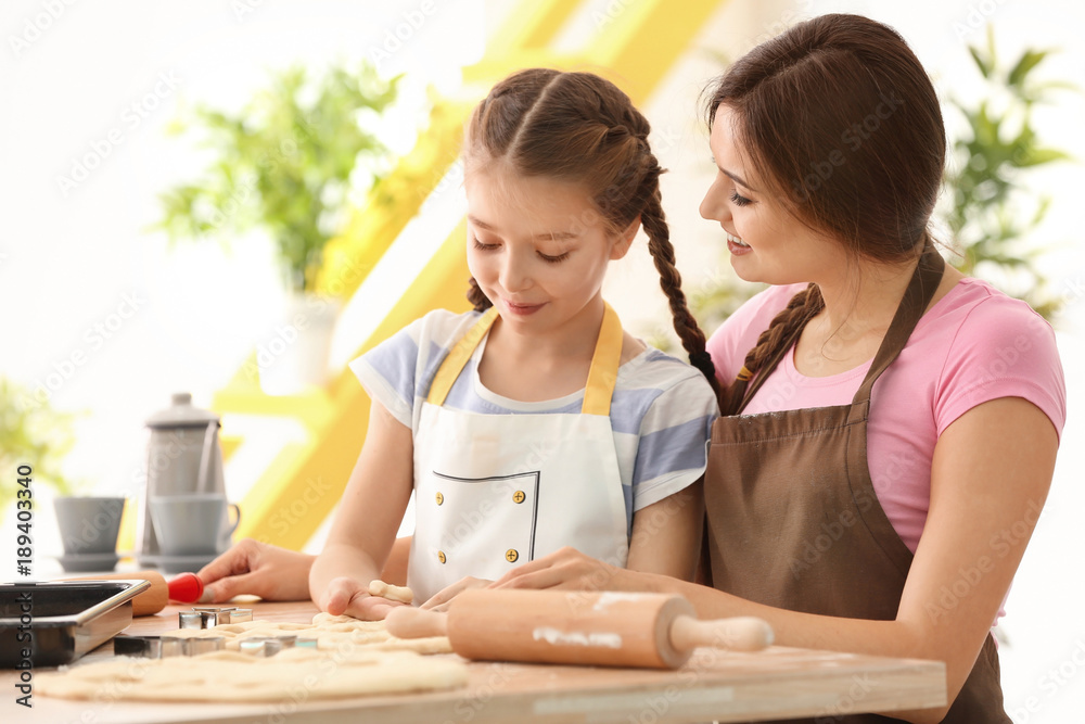 Mother and daughter with cookie dough at table indoors