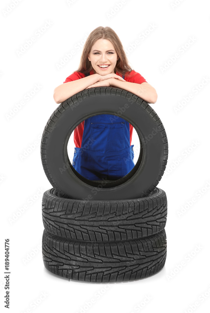 Female mechanic in uniform with car tires on white background