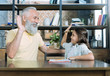 © zinkevych - Homework is done. Waist up shot of a positive minded elderly man and his cute little granddaughter grinning broadly while sitting at a table and high fiving.