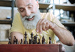 © zinkevych - Favorite leisure activity. Selective focus on a positive minded retired gentleman grinning broadly while sitting at a table and playing chess at home.