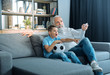 © zinkevych - Check that out. Serene elderly man relaxing on a sofa and changing channels with a remote control while his adorable grandson reactive to something emotionally.