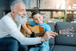 © zinkevych - Transmitting knowledge. Joyful senior man beaming while spending his time with an adorable grandson and showing him how to play guitar.