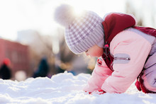 Small Child Crawls On Snow Against The Background Of A Sunset In Winter