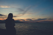 Silhouettes image of a woman looking at sea view on the beach with sunset background