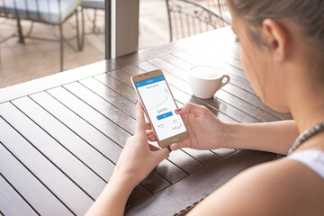 Poster - Monitoring the value of the crypto currency online with a mobile phone. Girl holding smart phone. Cup of coffee beside.
