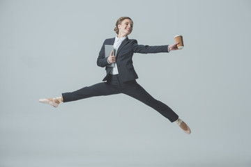 Wall Mural - businesswoman in suit and ballet shoes jumping with coffee and tablet, isolated on grey