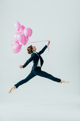 Wall Mural - businesswoman in suit and ballet shoes jumping with pink balloons, isolated on grey