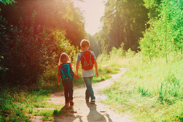 little boy and girl with backpacks walk in sunset nature