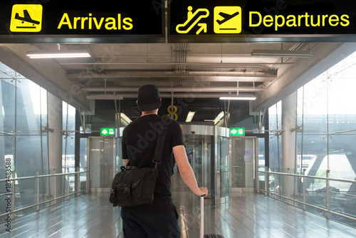 Cuadros en Lienzo Man in travel with suitcase in front of billboards of departures and arrival in