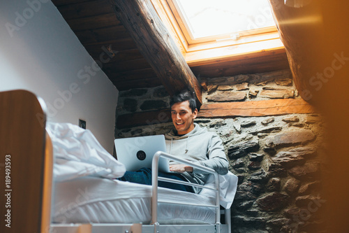 Fotografía Happy hostel visitor or tourist, satisfied traveler sits on top of bunk bed, rests after long day of adventures and exploring surfs internet to research new location