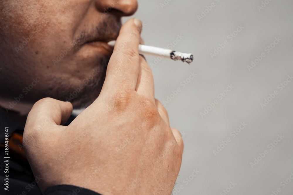 how to hold a cigarette in mouth A man with a burning cigarette in his mouth. Fingers of a hand hold a  cigarette. copy space Stock Photo