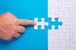 © azrisuratmin - Hand holding piece of white puzzle on blue background. Business and team work concept.